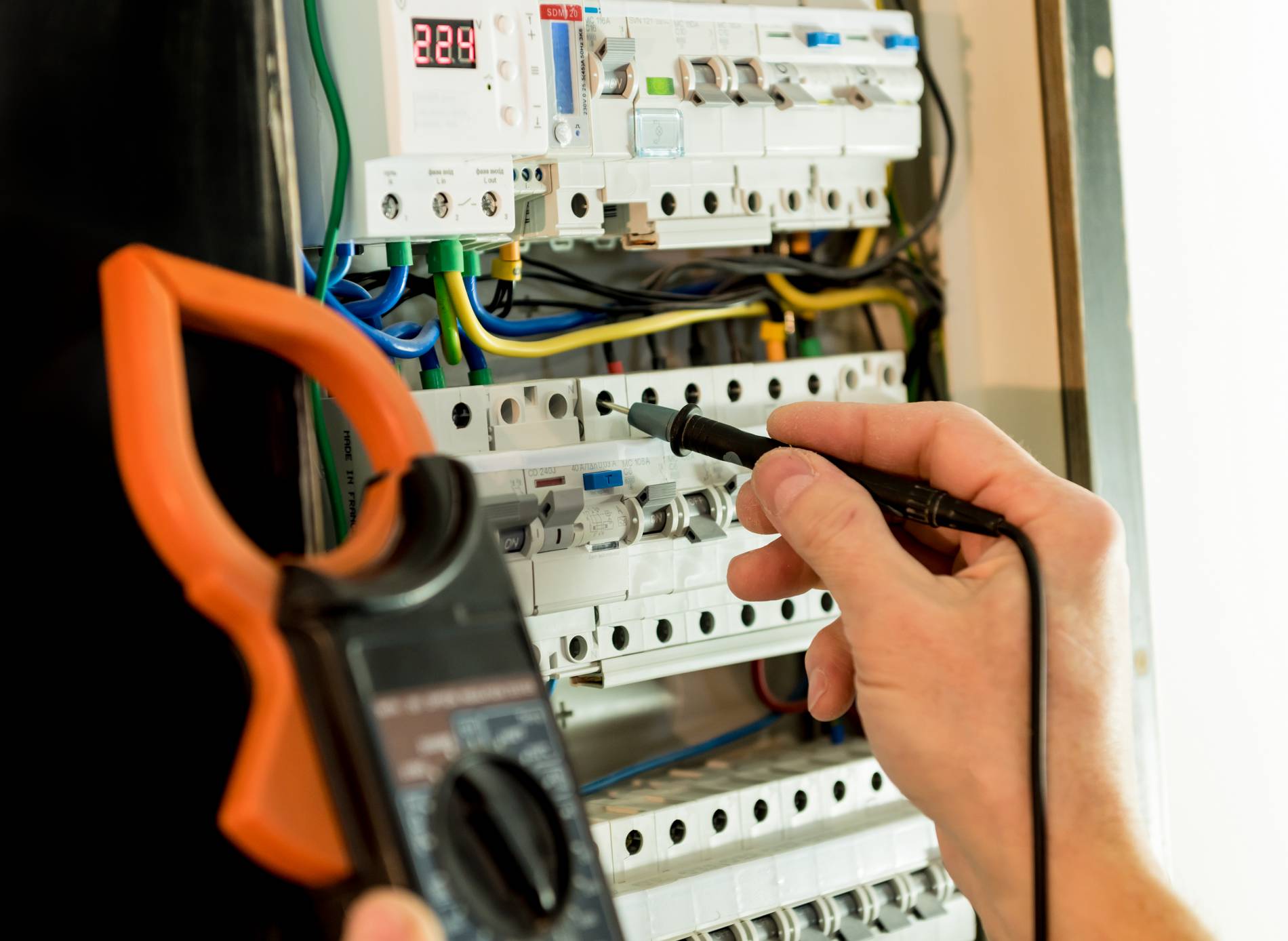 Électricien contrôlant un tableau électrique avec une pince ampèremétrique